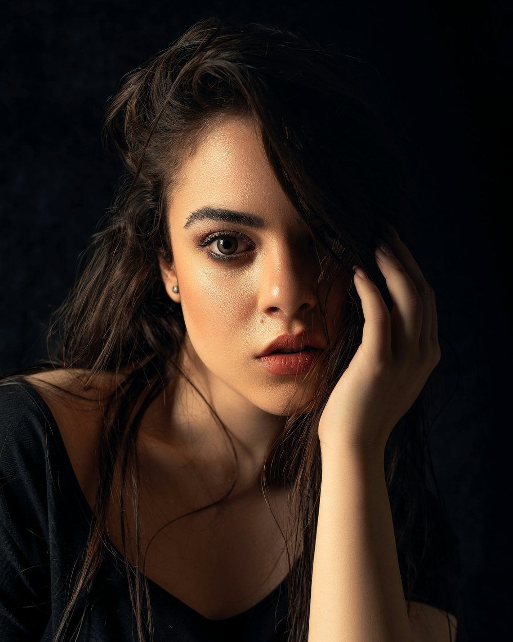 Portrait photo of a woman with long dark hair, one hand raised to her face.